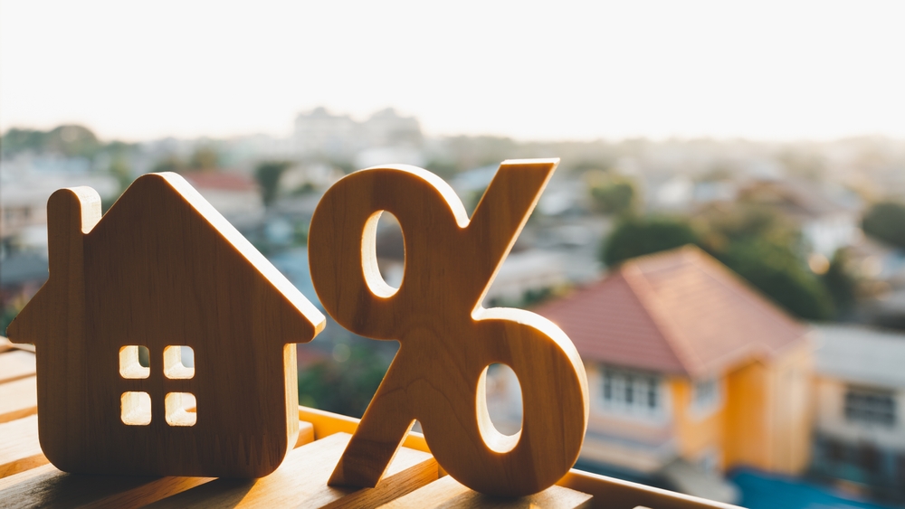 Wooden house model next to a percentage symbol, illustrating the concept of real estate investment and property market trends.